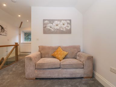 A beige sofa with a yellow cushion against a white wall with a floral painting in a hallway with grey carpet at Greenlawns Burnham-On-Sea