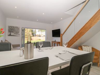 A dining table set with wine and glasses in a room with staircase and open doors to a garden at Greenlawns in Burnham-On-Sea