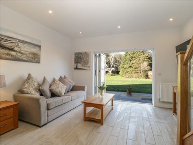 A living room with a sofa cushions wooden coffee table and side table with an open door leading to a garden at Greenlawns in Burnham-On-Sea