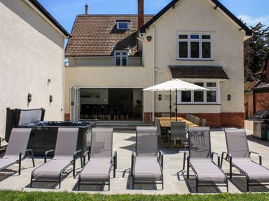 A backyard patio with sun loungers a dining table with umbrella a hot tub and a gas grill at Greenlawns in Burnham-On-Sea
