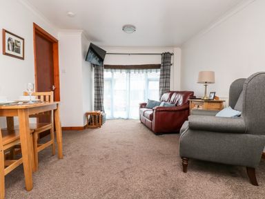A living room with a red sofa gray armchair wooden side table and dining table at Coach House Cottage in Bude
