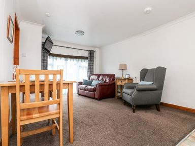 A dining table with chairs and a living area with a sofa and armchair at Coach House Cottage in Bude
