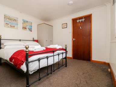 A bedroom with a black metal bed with white bedding and a red throw at Coach House Cottage in Bude