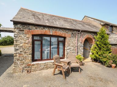 A stone cottage exterior with wooden chairs and a table outside at Coach House Cottage in Bude