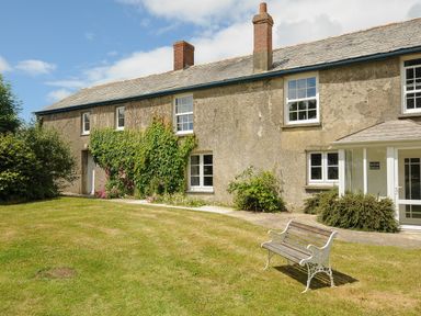 Exterior view of a farmhouse with windows bushes and a bench on the lawn at Lee Barton Farmhouse in Bude