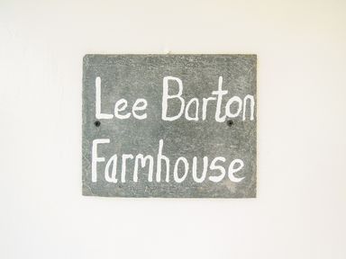 A slate sign with white writing saying Lee Barton Farmhouse on a white wall at Lee Barton Farmhouse Bude