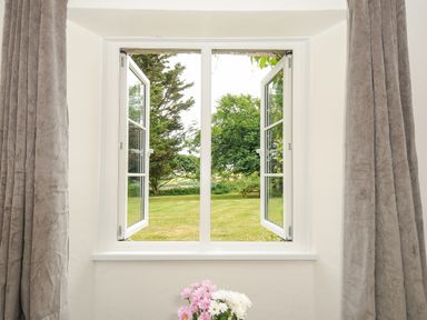 A window with open white frames looking out to a grassy garden with trees and a picnic table at Lee Barton Farmhouse in Bude