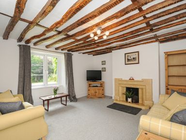 A living room with exposed wooden beams a stone fireplace two sofas a wooden coffee table and a television at Lee Barton Farmhouse in Bude