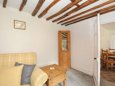 A sitting room with a yellow plaid sofa wooden corner cabinet and wooden table at Lee Barton Farmhouse in Bude