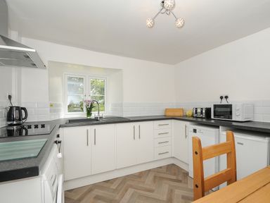 A kitchen with white cabinets black countertops and a window above the sink at Lee Barton Farmhouse in Bude