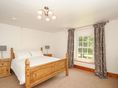 A bedroom with a wooden bed and two bedside tables with lamps near a window with curtains at Lee Barton Farmhouse in Bude