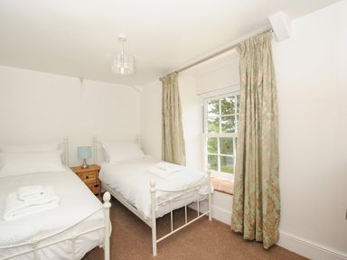 A bedroom with two single beds a wooden nightstand with a lamp and a window with curtains at Lee Barton Farmhouse in Bude