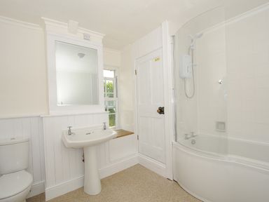A bathroom with a toilet sink mirror window door and bathtub with shower at Lee Barton Farmhouse in Bude