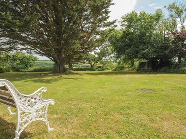 A garden with a large tree a white bench and a picnic table at Lee Barton Farmhouse in Bude