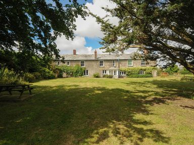 A large grassy garden with trees and a picnic bench in front of a farmhouse at Lee Barton Farmhouse in Bude