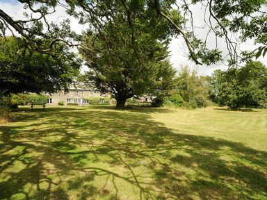 A large lawn with trees and a stone building in the background at Lee Barton Farmhouse Bude