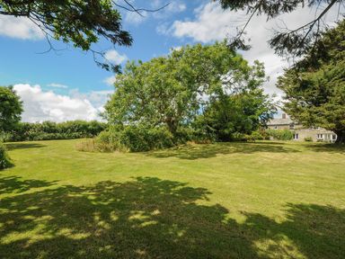 A grassy garden area with trees and a stone house in the background at Lee Barton Farmhouse in Bude