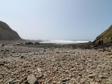 A rocky beach with waves in the background and cliffs on both sides at Lee Barton Farmhouse in Bude