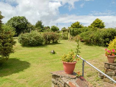 A garden with grass, bushes, a wooden swing, and flower pots on stone ledges at The Roundhouse in Bude