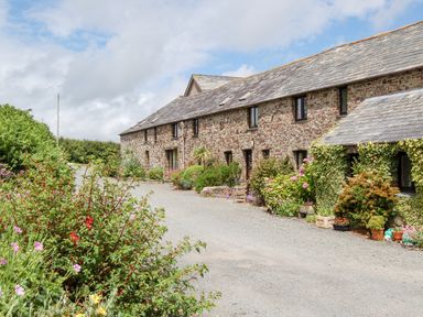 A stone building with multiple windows and plants along a gravel driveway at The Roundhouse in Bude