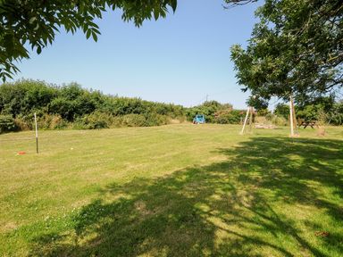 A grassy garden area with a swing set a golf hole a blue toy tractor and a picnic bench at The Roundhouse in Bude