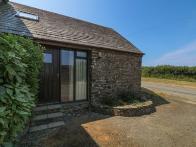 The exterior of a stone house with a wooden door and window next to a small garden bed and a hedge at The Roundhouse in Bude