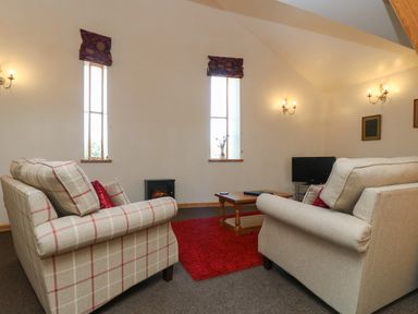 A living room with two sofas a wooden coffee table a red rug and a small television at The Roundhouse in Bude