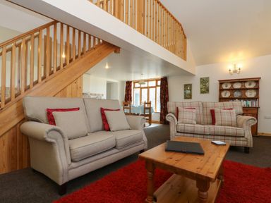 A living room with two sofas red pillows a wooden coffee table red rug and wooden stairs at The Roundhouse in Bude