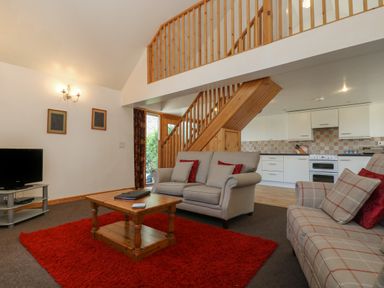A living room with sofas a wooden coffee table a red rug a television and a staircase leading to an upper floor at The Roundhouse in Bude