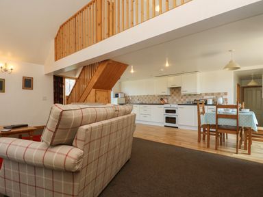 An open living area with a plaid sofa wooden dining table and chairs kitchen cabinets and stairs at The Roundhouse in Bude