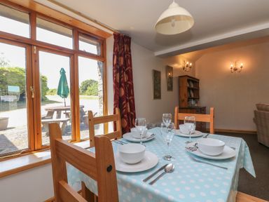 A dining area with a table set for four next to a large window with a red curtain and wooden chairs at The Roundhouse in Bude