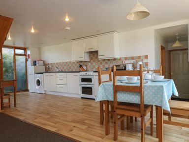 A kitchen and dining area with wooden chairs and table with blue polka dot tablecloth at The Roundhouse in Bude