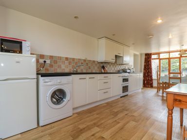 A kitchen with refrigerator microwave washing machine stove and dining table near window at The Roundhouse in Bude