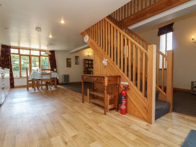 A dining area with wooden table and chairs near a large window and wooden staircase with a small table and fire extinguisher at The Roundhouse in Bude