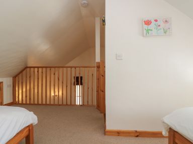 An attic room with beige carpet and wooden railing and two beds at The Roundhouse in Bude