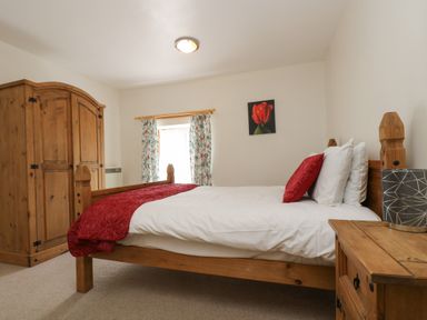 A bedroom with a wooden bed red bedding a wooden wardrobe and a wooden nightstand at The Roundhouse in Bude