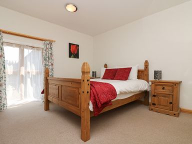 A bedroom with a wooden bed with red cushions and blanket a wooden bedside table and a window with floral curtains at The Roundhouse in Bude