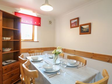 A dining room with a table set for four by a window with a red blind at Swallow Cottage in Bude