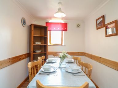 A dining room with a set dining table wooden chairs and a shelving unit at Swallow Cottage in Bude