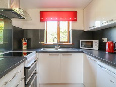A kitchen with a stove sink microwave and kettle at Swallow Cottage in Bude