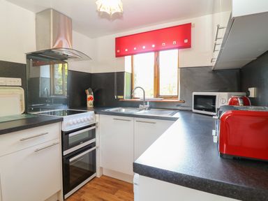 A kitchen with white cabinets black countertops a stove a sink and red appliances at Swallow Cottage in Bude
