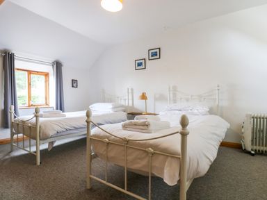 A bedroom with two single beds white bedding and towels a window with gray curtains and a bedside table with a lamp at Swallow Cottage in Bude