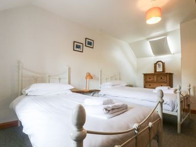 A bedroom with two single beds white bedding a wooden dresser and a small orange lamp at Swallow Cottage in Bude