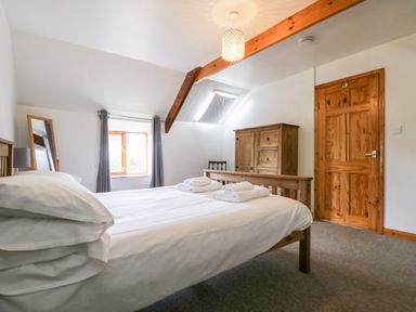 A bedroom with a wooden bed with white bedding and towels a wooden wardrobe a wooden door and a window with curtains at Swallow Cottage in Bude