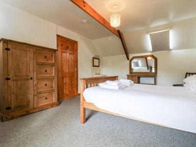A bedroom with a wooden bed and furniture including wardrobe dresser and mirror at Swallow Cottage in Bude