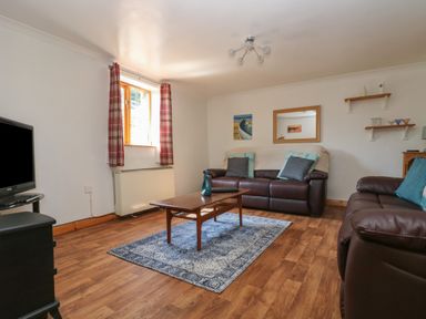 A living room with two leather sofas a wooden coffee table a television and a window with red curtains at Swallow Cottage in Bude