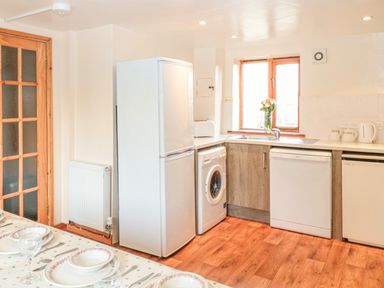 A kitchen with fridge washing machine dishwasher and wooden floor at The Wagon Linney in Bude
