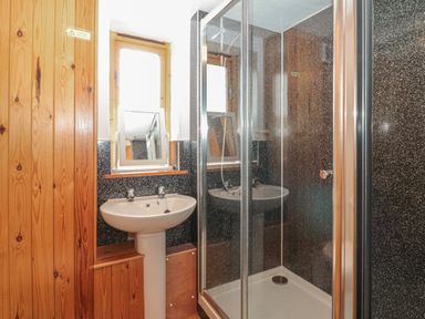 A bathroom with a pedestal sink and a corner shower with glass doors and a small window at The Wagon Linney in Bude