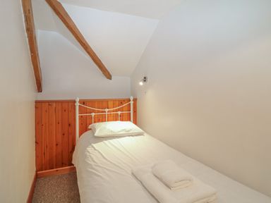A small bedroom with a single bed white bedding wooden paneling and exposed ceiling beams at The Wagon Linney in Bude