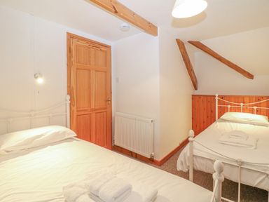 A bedroom with two single beds with white bedding wooden door and exposed wooden beams at The Wagon Linney in Bude